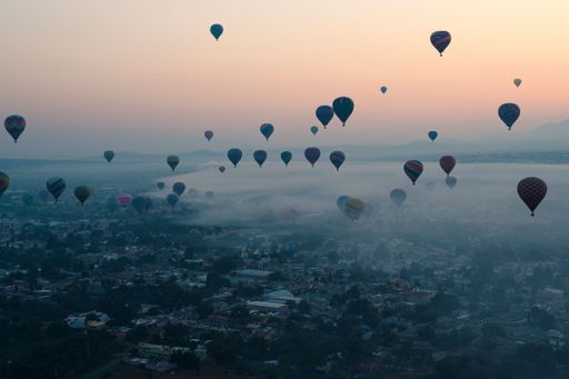 An aerial shot of colorful hot air balloons flying high above the city skyline at sunset.