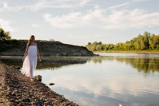 A young attractive blonde with a white dress walking on the shore of a calm lake