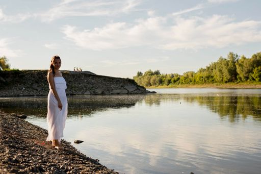A beautiful Caucasian woman wearing a white dress while standing on the bank of the river