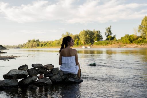 A beautiful Caucasian woman in a white dress sitting on a rock in a river