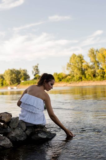 A vertical shot of a beautiful caucasian female in a white dress posing near a lake