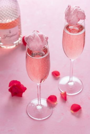 Two glasses of pink champagne with cotton candy and rose flower petals on a pink background