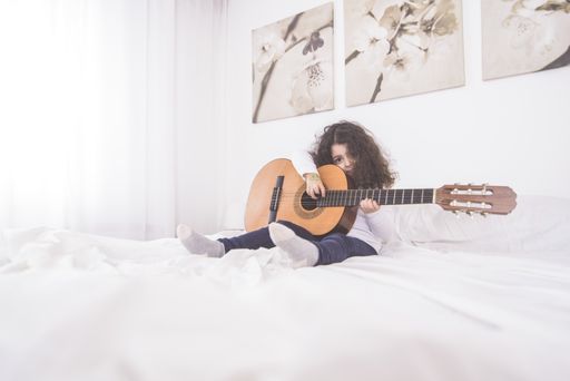 A closeup shot of a cute Caucasian little girl sitting in a bed with a guitar in her hands