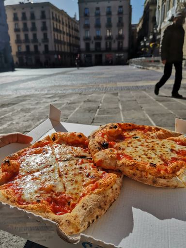 A vertical shot of a delicious pizza in a box being served in the street