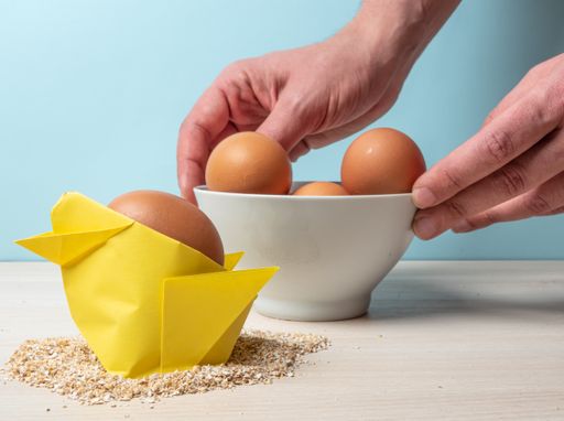 A closeup shot of a yellow origami chicken and eggs on a blue wall background