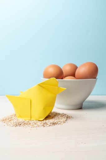 A vertical shot of a yellow origami chicken and eggs on a blue wall background