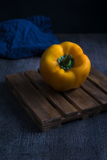 A vertical shot of a sweet yellow pepper on a wooden board