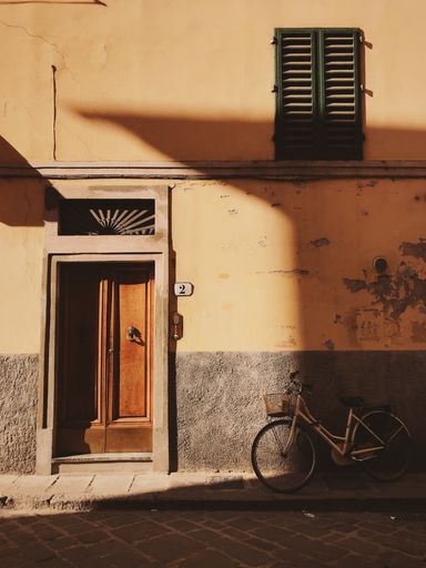A vertical shot of a vintage bicycle leaning against an old weathered wall at the entrance to the house