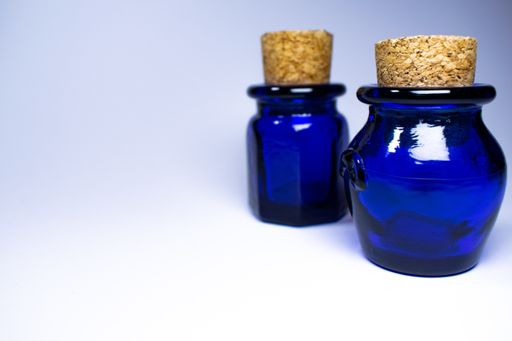 Two differently shaped blue empty bottles with cork stoppers and white gradient background