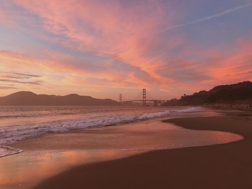 A majestic pink sunset cloudscape over wavy seawater with the Golden Gate Bridge on the horizon