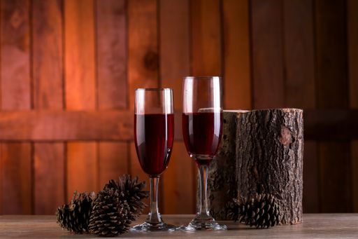 A selective focus shot of two glasses of red wine with pine cones and stumps on a wooden background