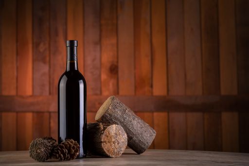A selective focus shot of a wine bottle with pine cones and stumps on a wooden background