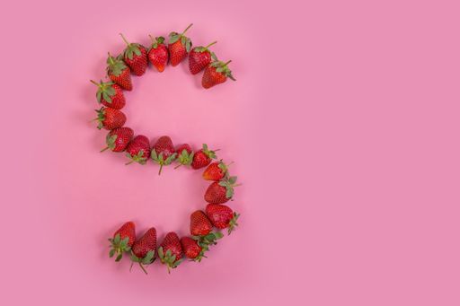 A top view of the S letter made of fresh strawberries on pink background