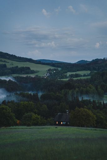 A vertical shot of a small mountain house with trees under blue cloudy sky in a valley