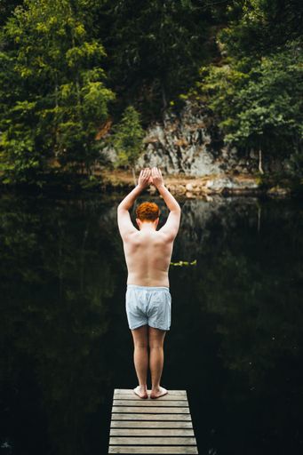 A back view of a ginger man in shorts getting ready to jump into the lake from a wooden springboard