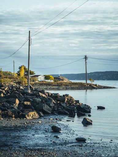 A vertical shot of utility poles on the rocky lakeshore against blue cloudy sky
