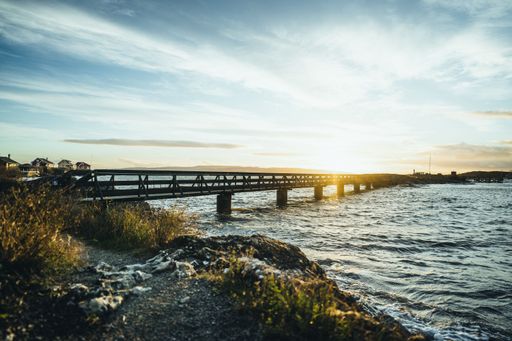 The bright sun in blue cloudy shining behind a long footbridge over the sea