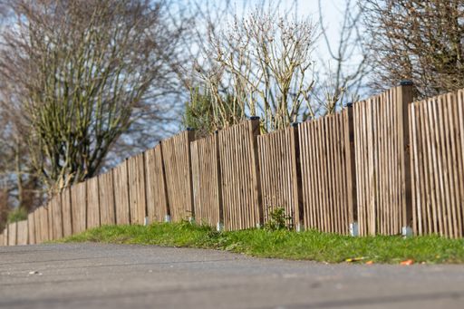 A landscape shot of a brown wooden fence of a mini forest with a clear blue sky