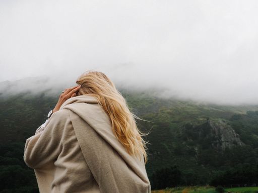 A rear view of a blonde woman having a phone call against a fog-covered mountain