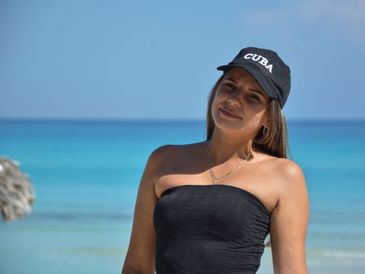 A young female standing at the beach and wearing a black swimsuit and hat