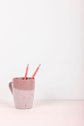 A close-up of two pink pencils lying in a white pink on a table isolated in a white background