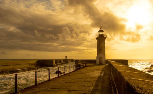 A lighthouse situated at the end of a long pier on the background of a dreamy cloudy sky