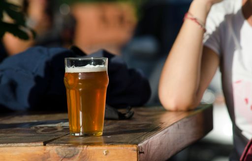 A young woman sitting next to a glass of beer on a wooden table