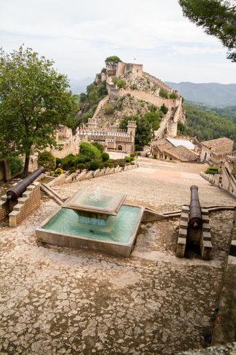 A vertical shot of historical monument Castillo de Jativa in Spain with water fountain and cannons in the foreground