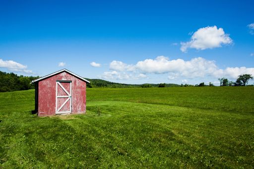 An old red storage in the middle of a field on a sunny day