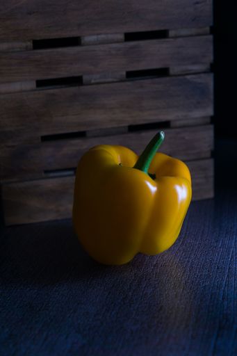 A vertical closeup shot of a yellow capsicum pepper against a wooden crate background