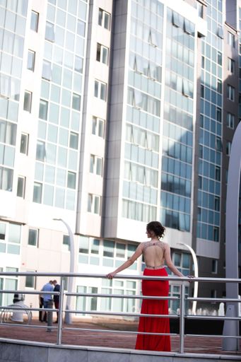 A vertical shot of a beautiful Caucasian female in an elegant open back red dress posing outdoors