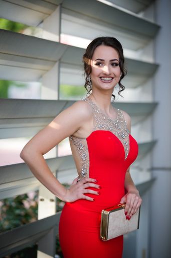 A vertical shot of a beautiful Caucasian female in an elegant red dress posing outdoors