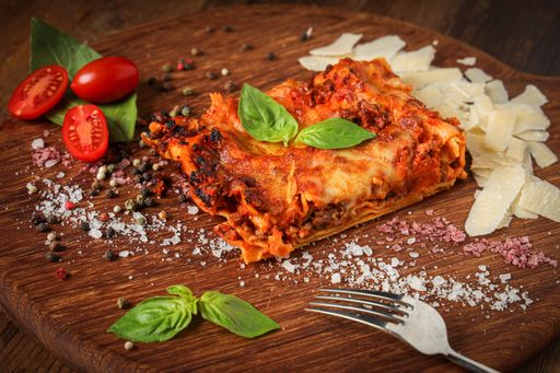 A closeup shot of a delicious gourmet slice of lasagna bolognese on a wooden board