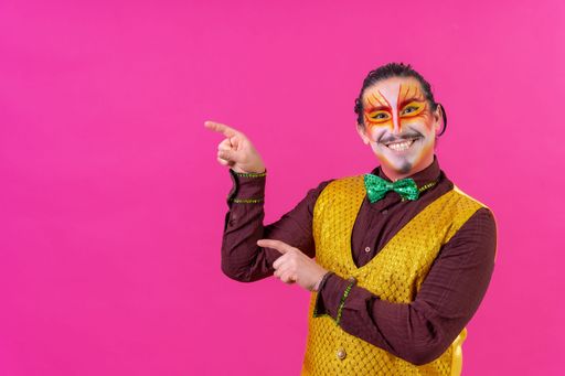 A cheerful circus performer pointing on an empty pink background for copyspace