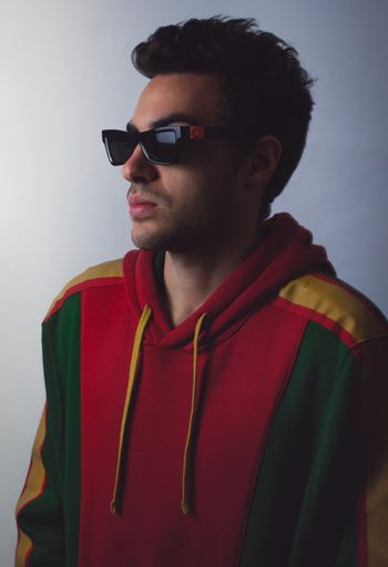 A vertical shot of a young male with sunglasses on a white wall