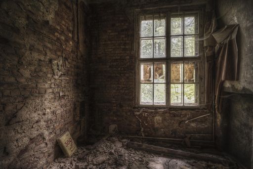 A beautiful shot of a window in a brick wall with a messy floor of an old room