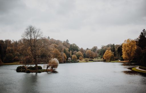 A majestic nature scene of a small reflective lake surrounded by colorful autumn vegetation