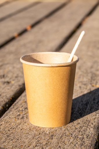 A vertical shot of a brown paper cup with a stick on a wooden surface