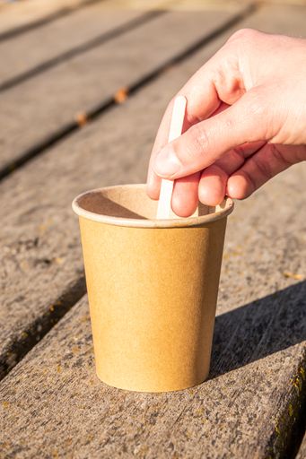 A vertical shot of a person mixing coffee with milk in a cup with a spoon outdoors