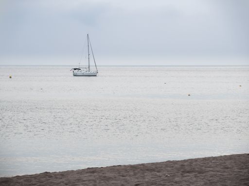 A boat in a calm sea captured from the beach on a cloudy day