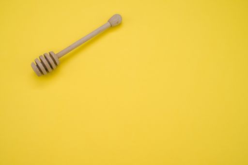 A high angle shot of a wooden honey dipper on a yellow surface