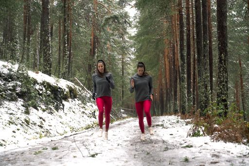 Young athletic female twins in sports outfits running in a forest covered with snow in the early morning