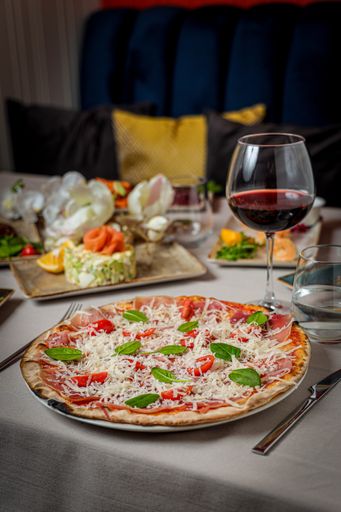 A vertical shot of pizza with vegan ingredients served with a glass of wine and salad in restaurant