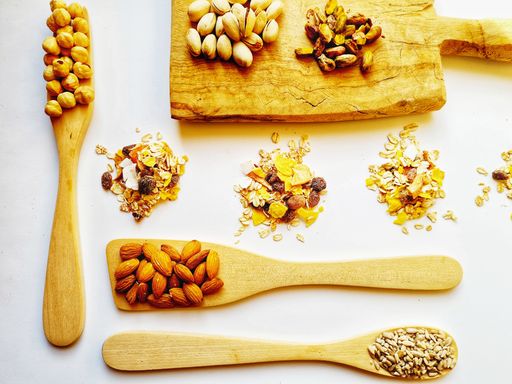 A cutting board and wooden ladles containing healthy nuts and seeds
