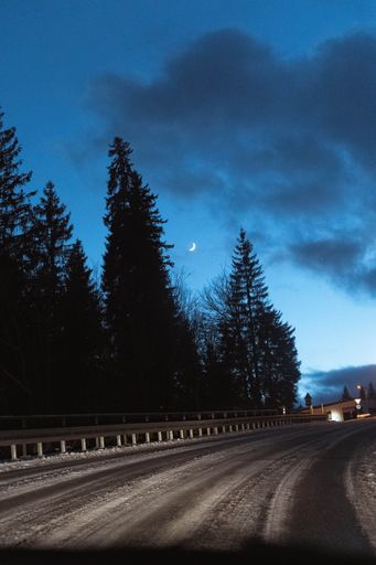 The night sky and moon shining brightly over a snow-covered winding road