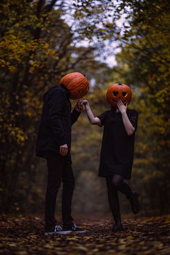 This Halloween, two people are walking through a forest wearing pumpkin head masks