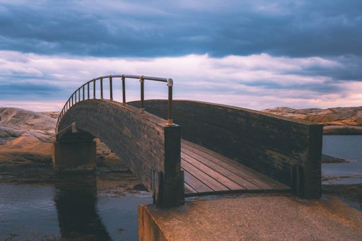 This beautiful image features a small wooden bridge over water next to rocks on the shore