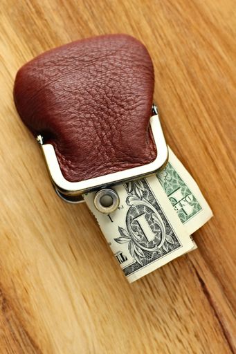 A vertical high angle shot of some dollar bills in a leather change purse on a wooden surface