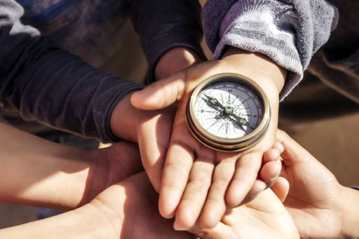 A group of children's hands holding a compass - teamwork concept
