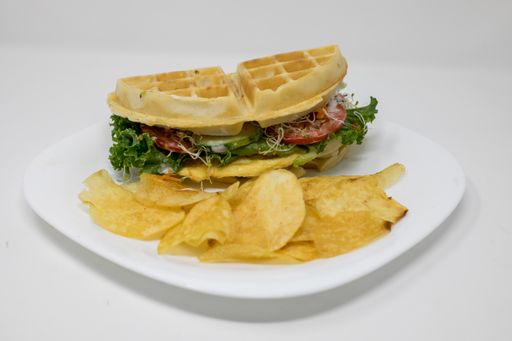 A closeup shot of a delicious waffle sandwich and potato chips on a white plate